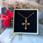 Gold cross necklace with red gemstones in a box with a red bow in the background