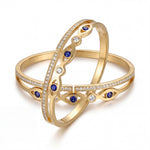 Gold bangles with blue gemstones and clear stones on a white background