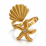 A gold-plated ring featuring a textured starfish with a clear round-cut gemstone at its center, layered with a shell-shaped element on a polished band, set against a clean white background.