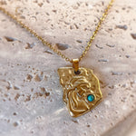 Gold necklace with a unique pendant on a textured beige surface