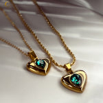 Two green crystal heart necklaces with different chain styles, displayed on a soft background