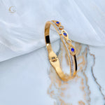 Side view of gold hinged bangle with navy Evil Eye crystals and clear zirconia on marble background.