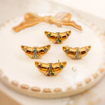 Close-up of four gold croissant-shaped earrings with cubic zirconia on a soft white surface