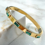Close-up side view of emerald crystal gold bangle bracelet, highlighting its glossy finish and stone detailing.