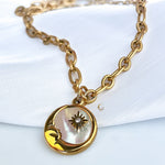 Close-up of Lyra necklace with crescent moon and northern star pendant on mother-of-pearl base.