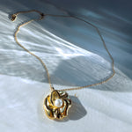 Close-up of Nymira gold flower necklace with pearl, lying on white stone