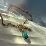 Gold chunky chain necklace with turquoise stone and feather charm displayed on pearly fabric