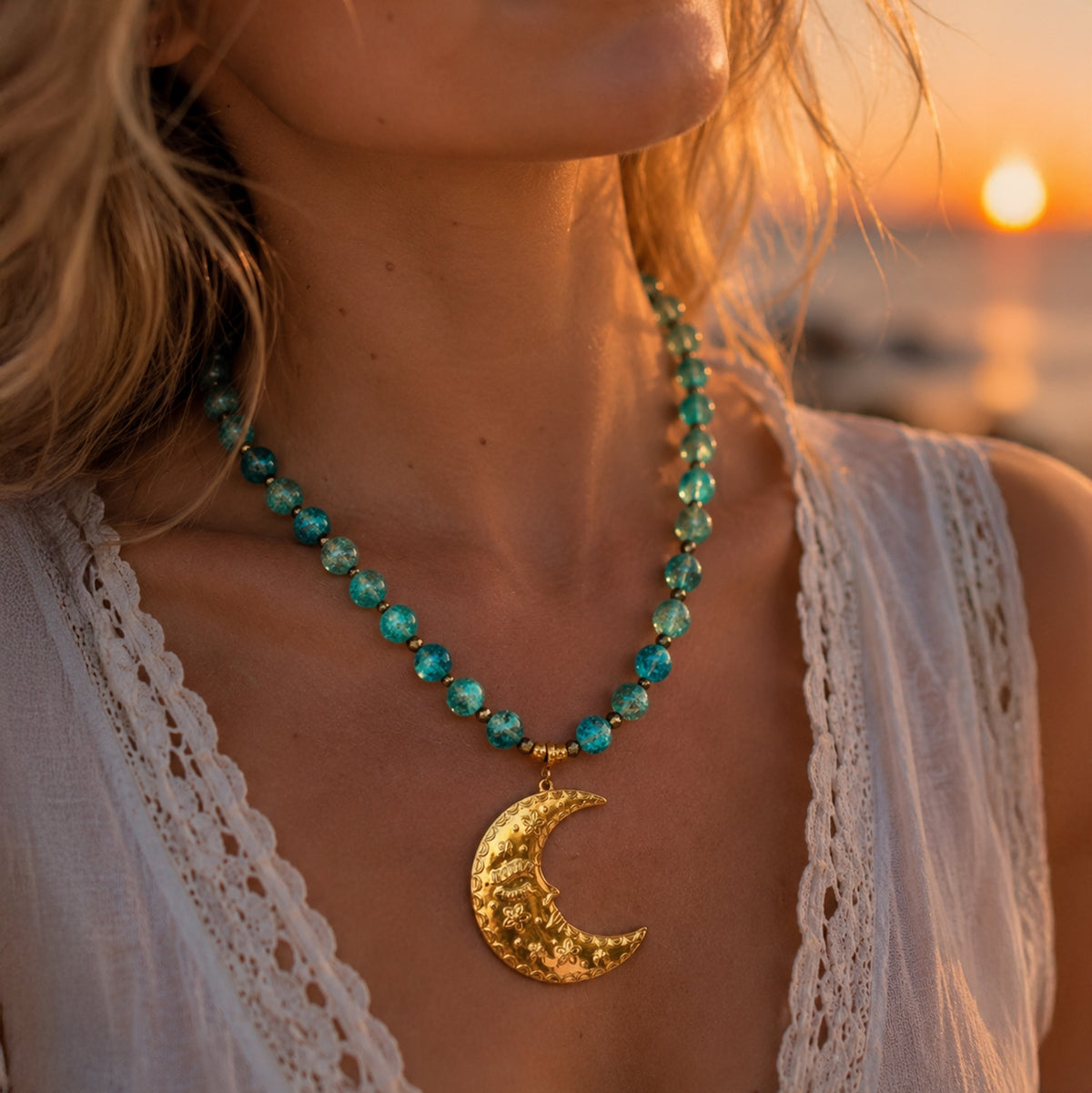 A close-up lifestyle shot of a woman wearing a beaded necklace with a gold crescent moon pendant, photographed during a warm sunset by the water.