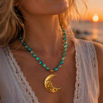 A close-up lifestyle shot of a woman wearing a beaded necklace with a gold crescent moon pendant, photographed during a warm sunset by the water.