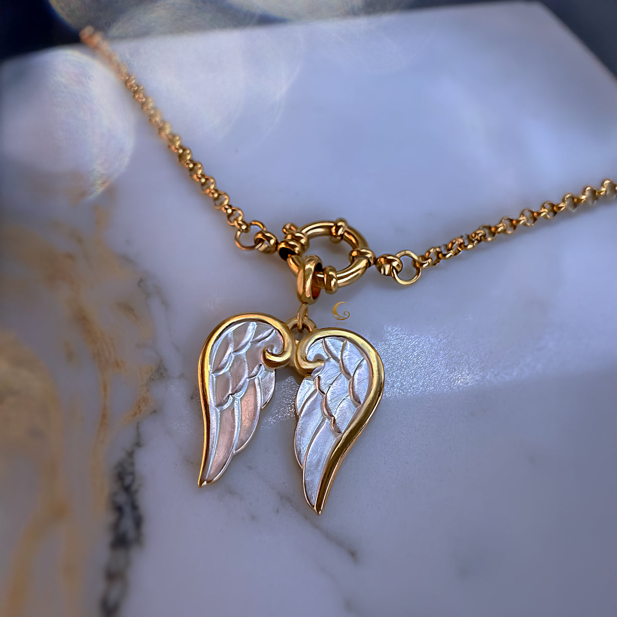 Gold necklace with angel wing pendant on a marble surface