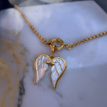 Gold necklace with angel wing pendant on a marble surface