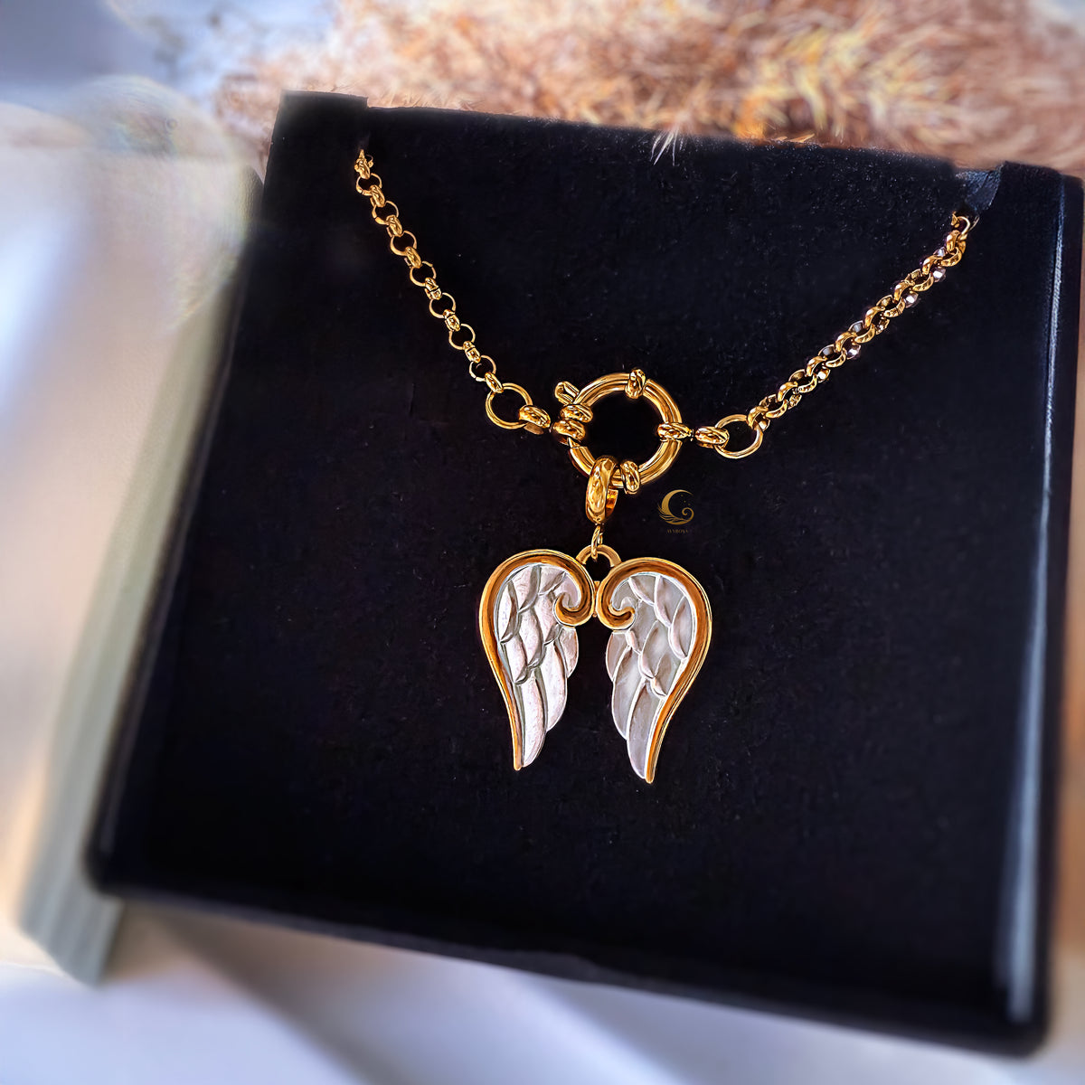 Gold and silver angel wing necklace on a black display stand.