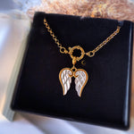 Gold and silver angel wing necklace on a black display stand.
