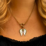 Gold necklace with a pendant shaped like angel wings worn by a person.