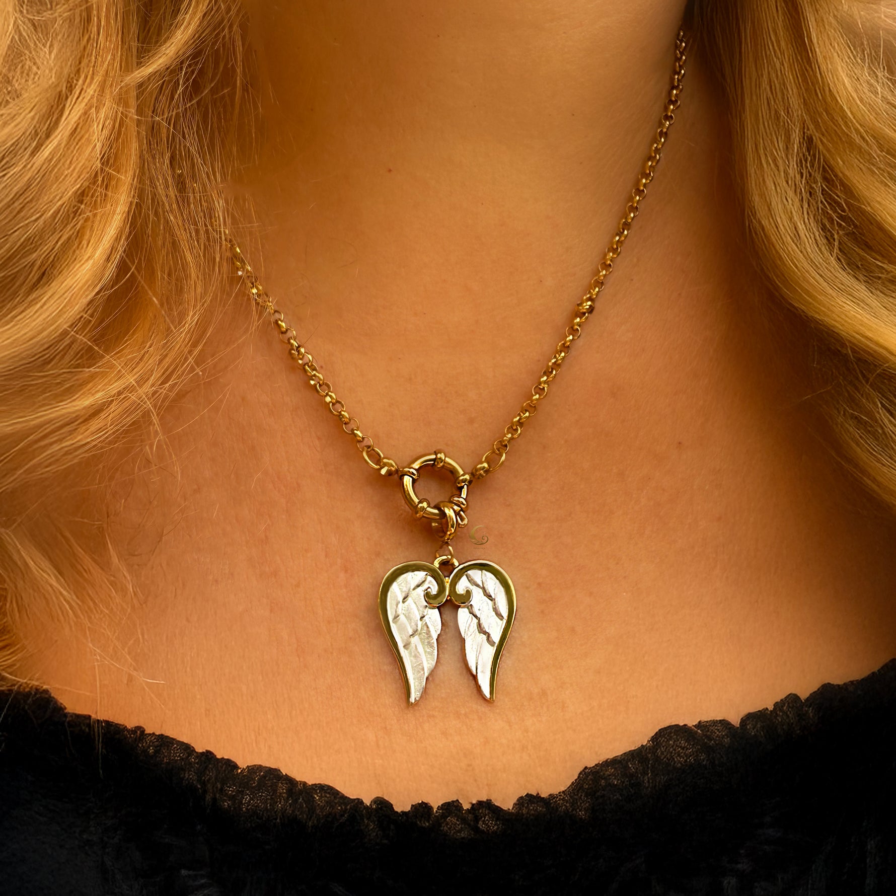Gold necklace with a pendant shaped like angel wings worn by a person.