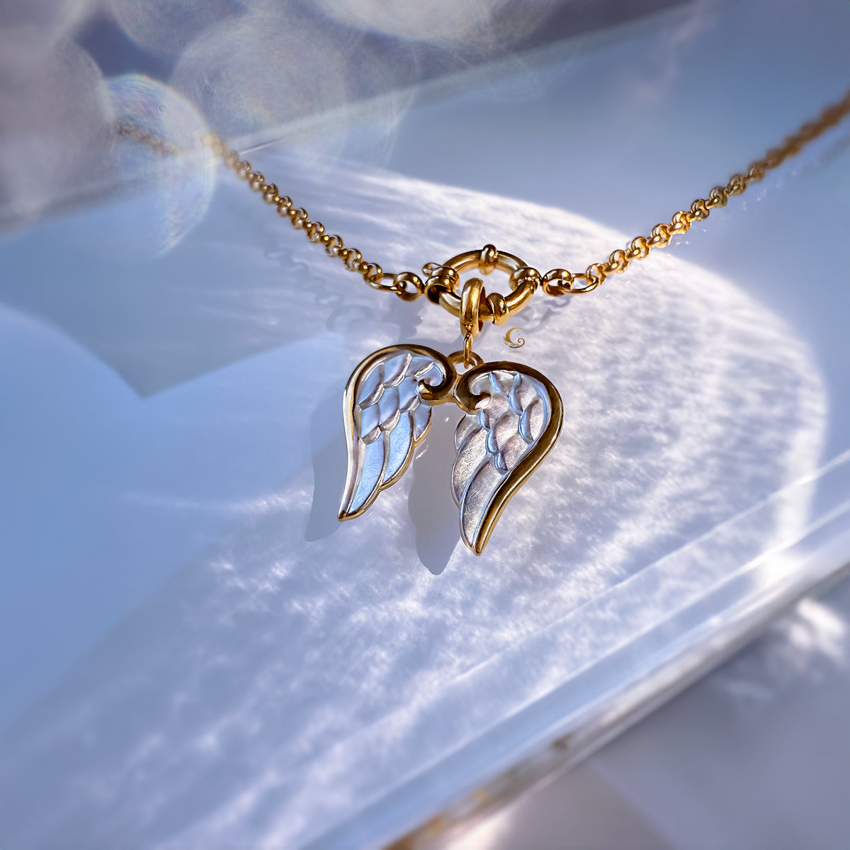 Gold and silver angel wing pendant on a chain against a light background