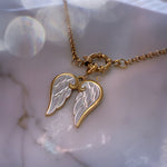 Gold and silver wing-shaped pendant on a chain against a marble background