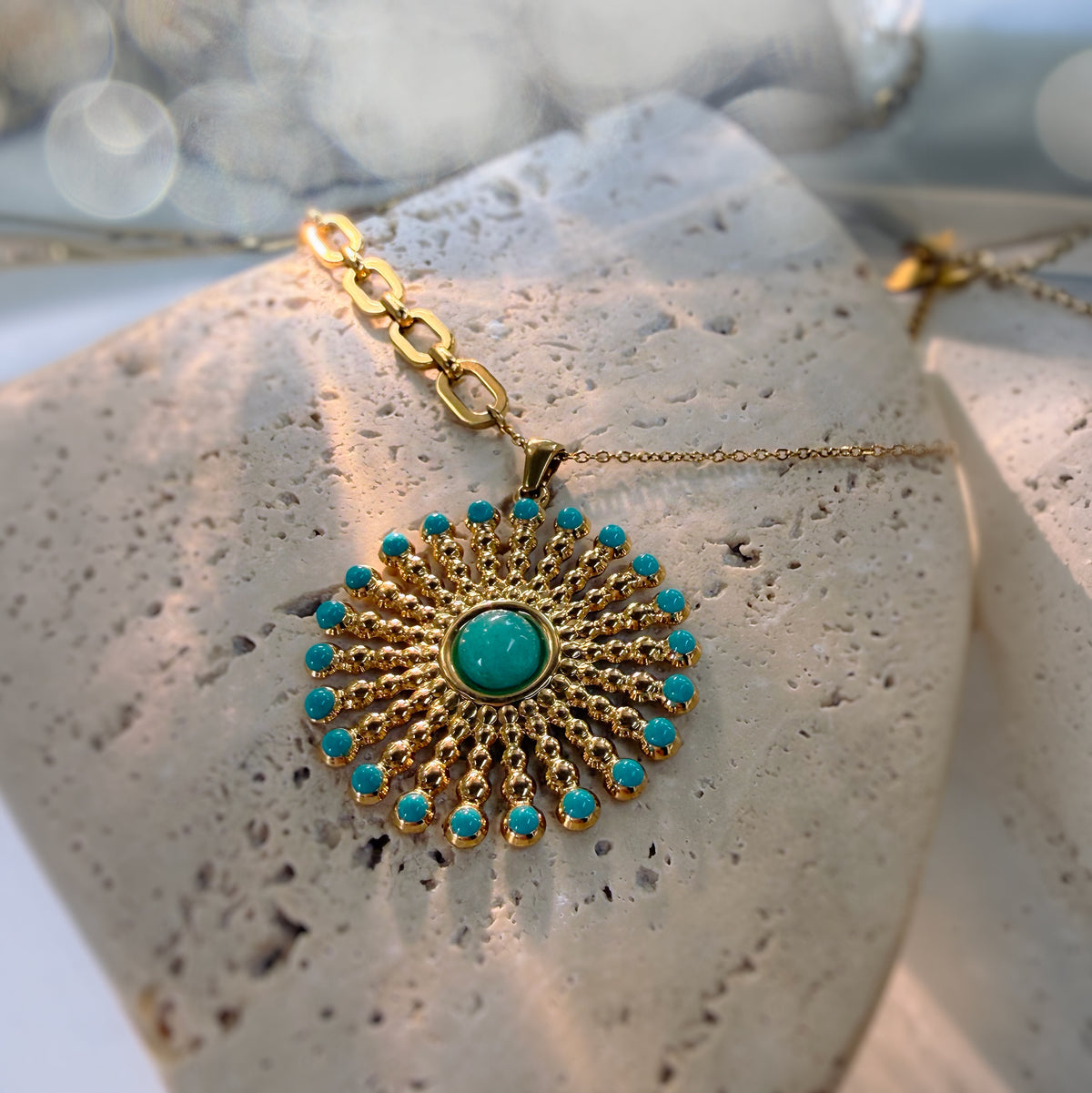 A gold pendant necklace with a turquoise center and surrounding turquoise stones, displayed on a textured stone surface.