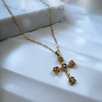 Gold cross necklace with a heart detail on a white surface
