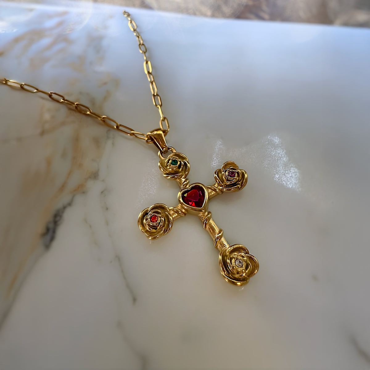 Gold cross necklace with red heart and rose details on a marble surface