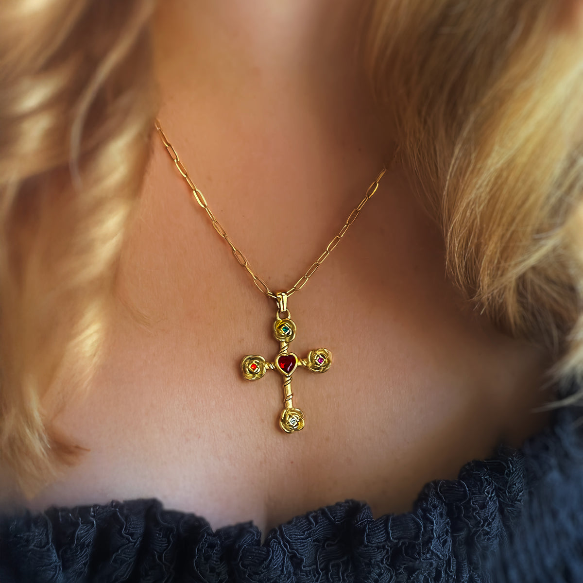 Gold cross necklace with colored stones worn by a person with blonde hair.