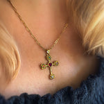 Gold cross necklace with colored gemstones worn by a person