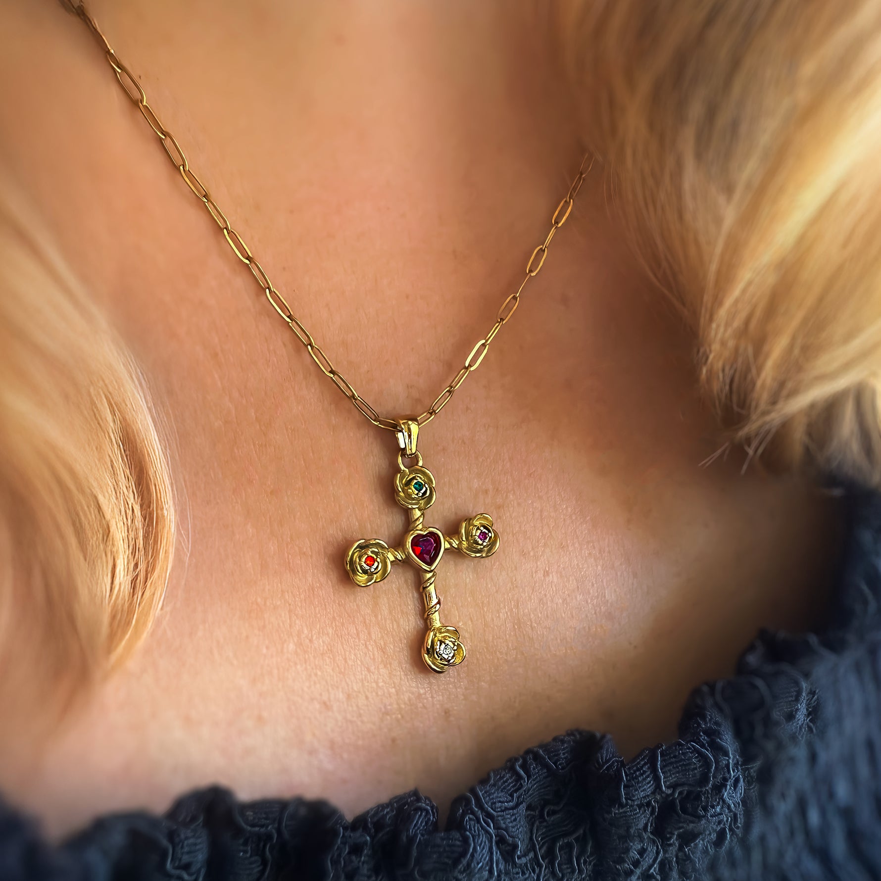 Gold cross necklace with colored gemstones worn by a person