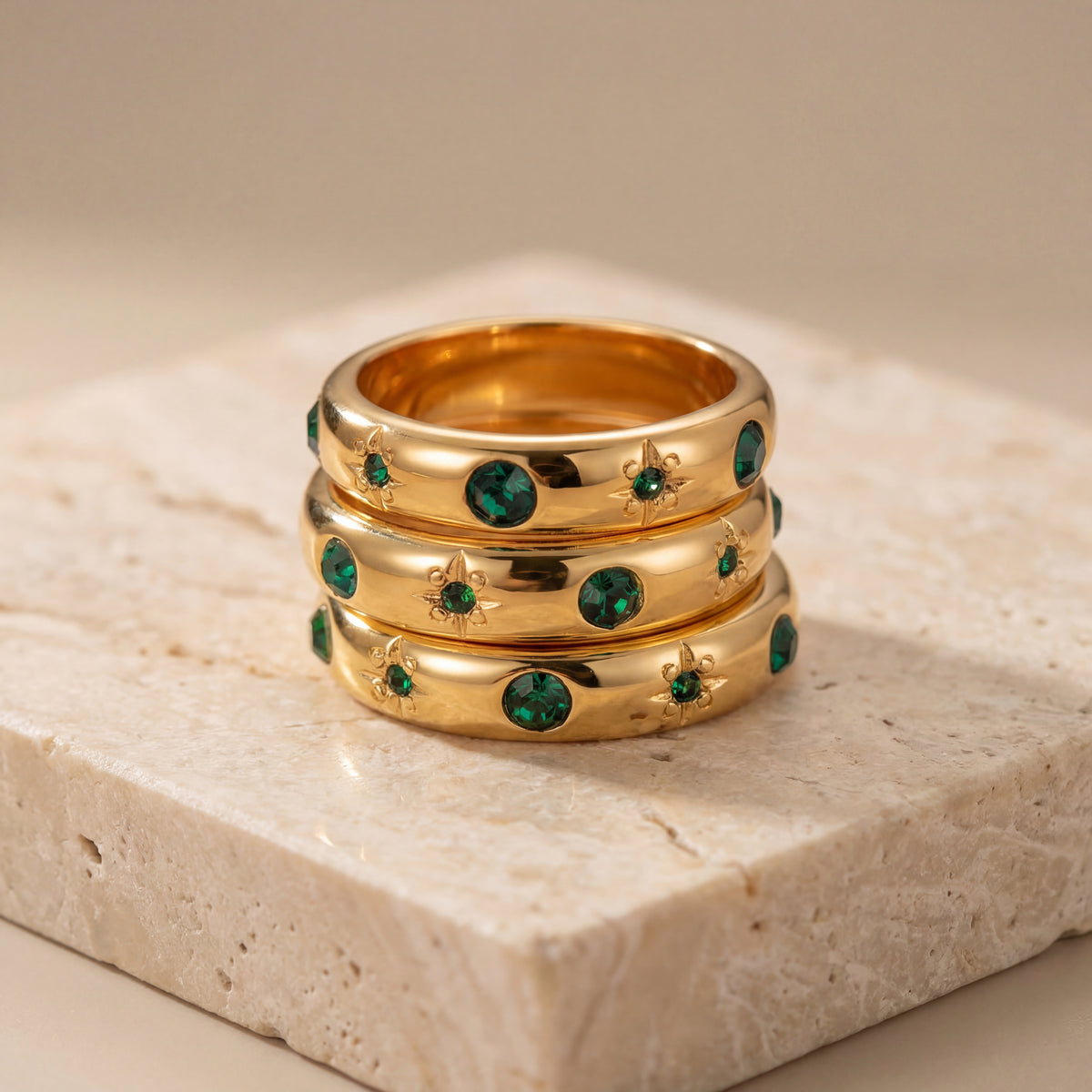 Three gold rings with green gemstones on a stone surface