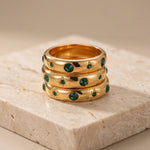 Three gold rings with green gemstones on a stone surface