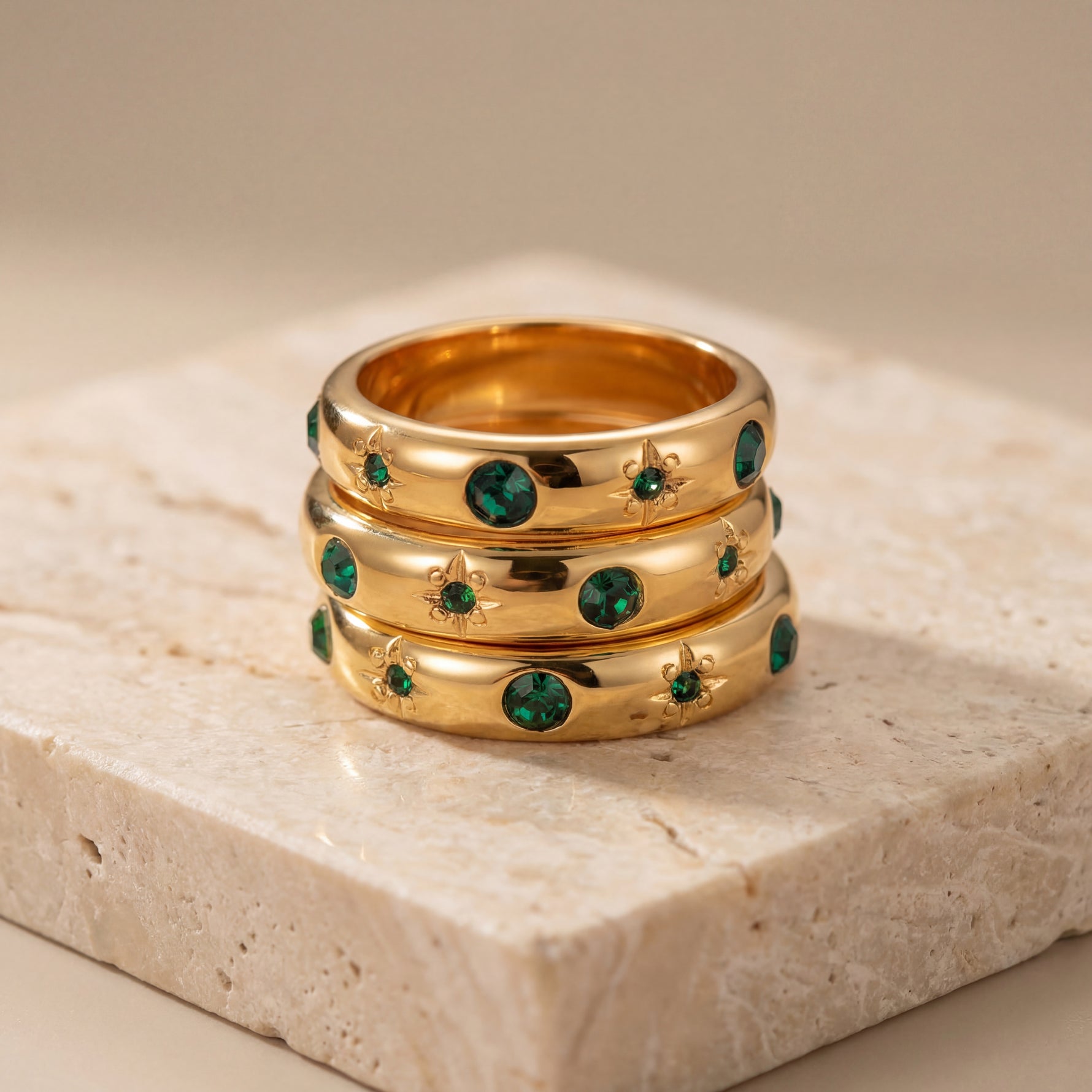 Three gold rings with green gemstones on a stone surface
