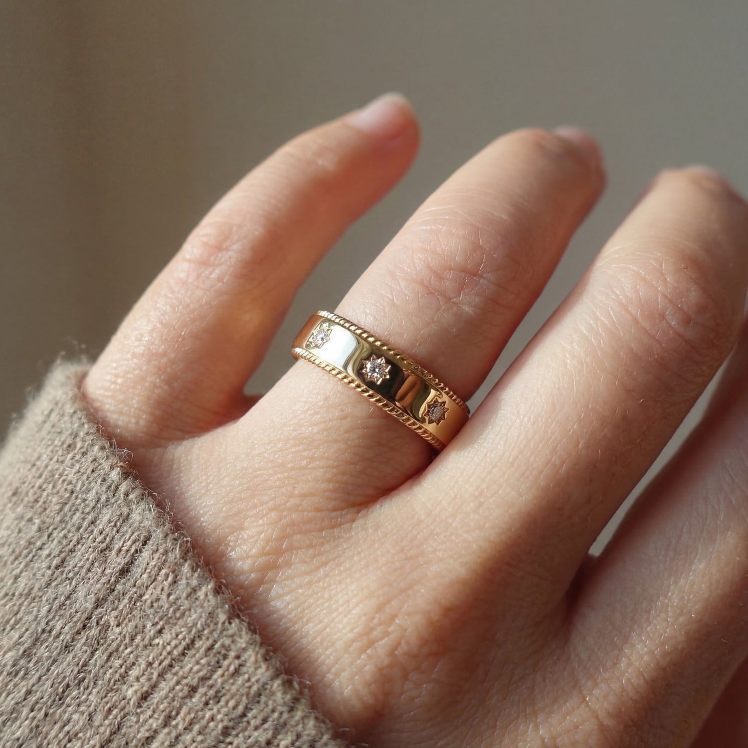 Close-up of a hand wearing a gold ring with embedded stones against a neutral background