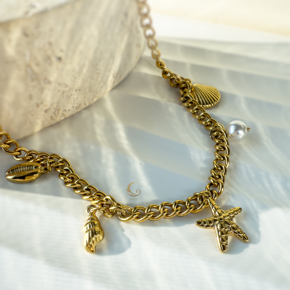 Detailed view of Halina necklace with golden starfish and vegan pearl charms lying on decorative stone background