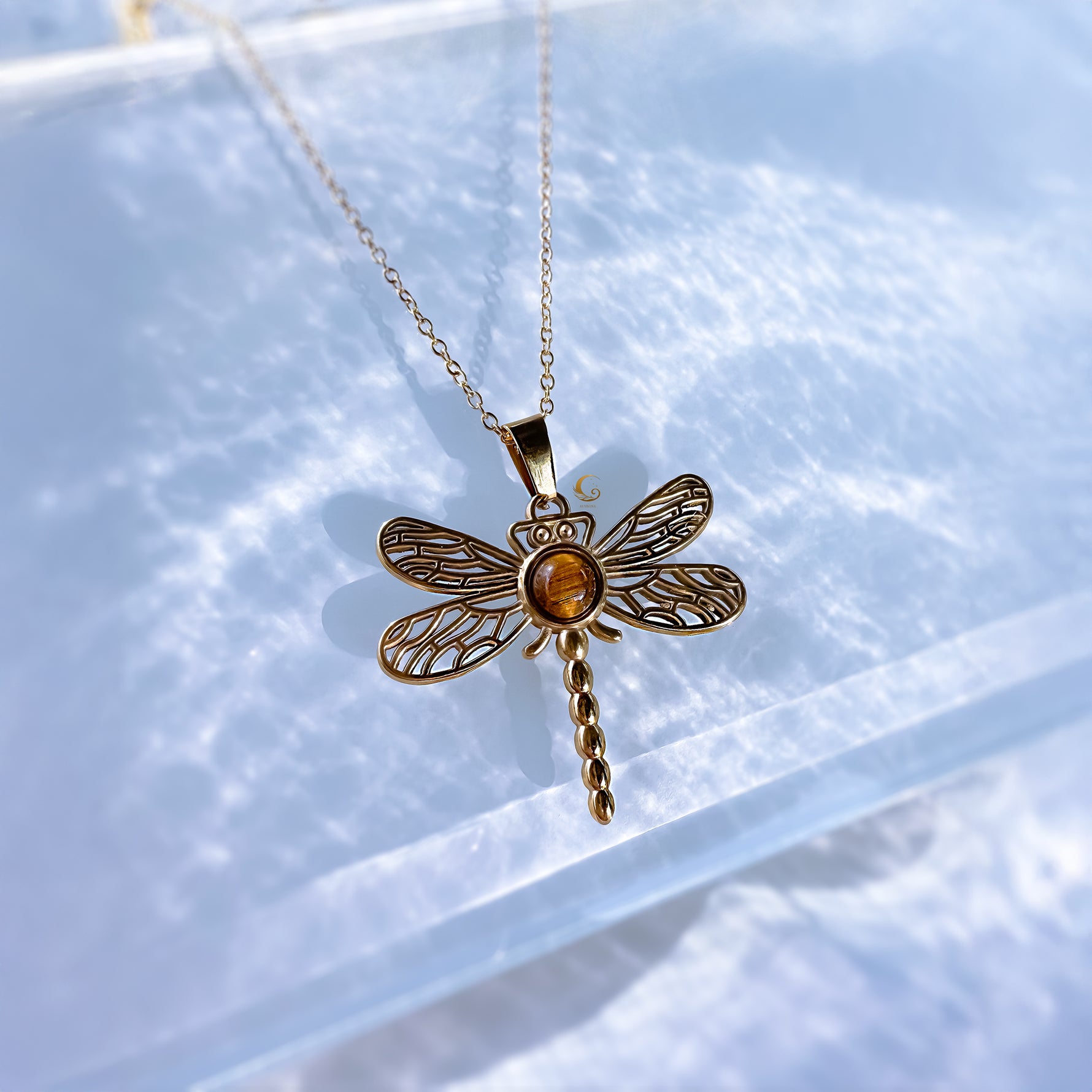 Gold dragonfly pendant necklace on a light blue background