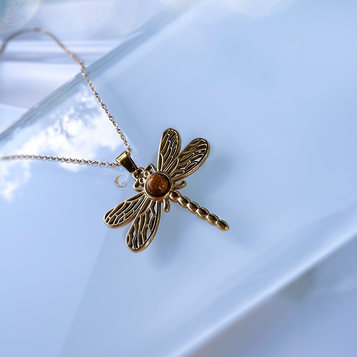 Gold dragonfly necklace with a brown gemstone on a light blue background