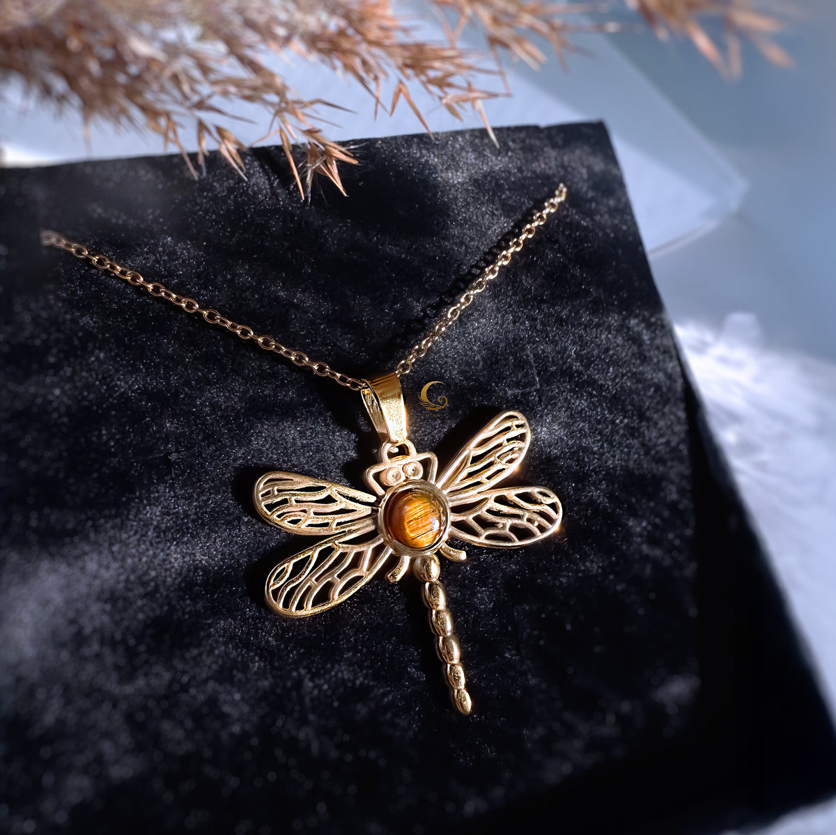 Gold dragonfly necklace with a yellow stone on a black surface