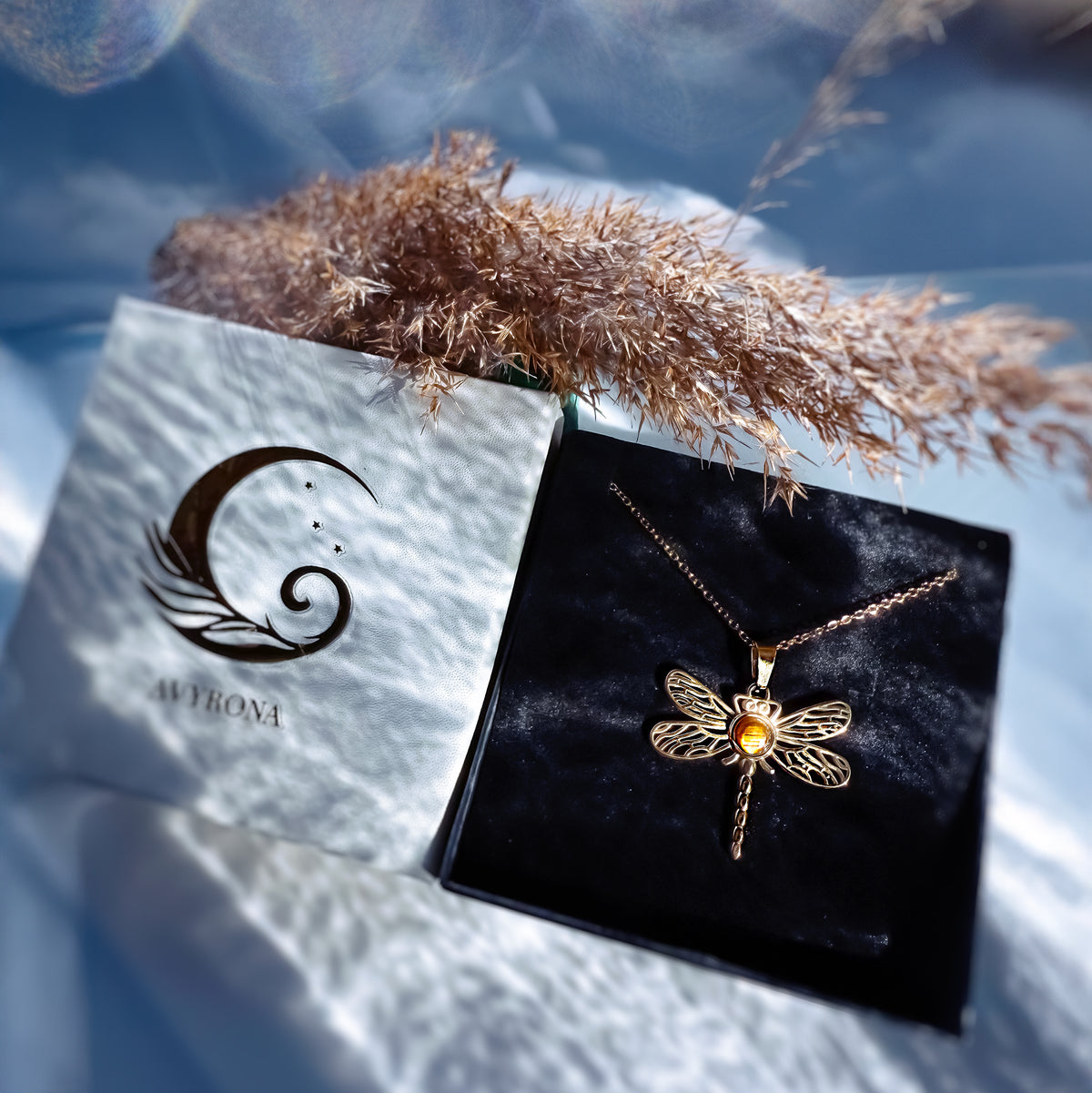 Gold dragonfly necklace on a black velvet pillow with a brand card in the background