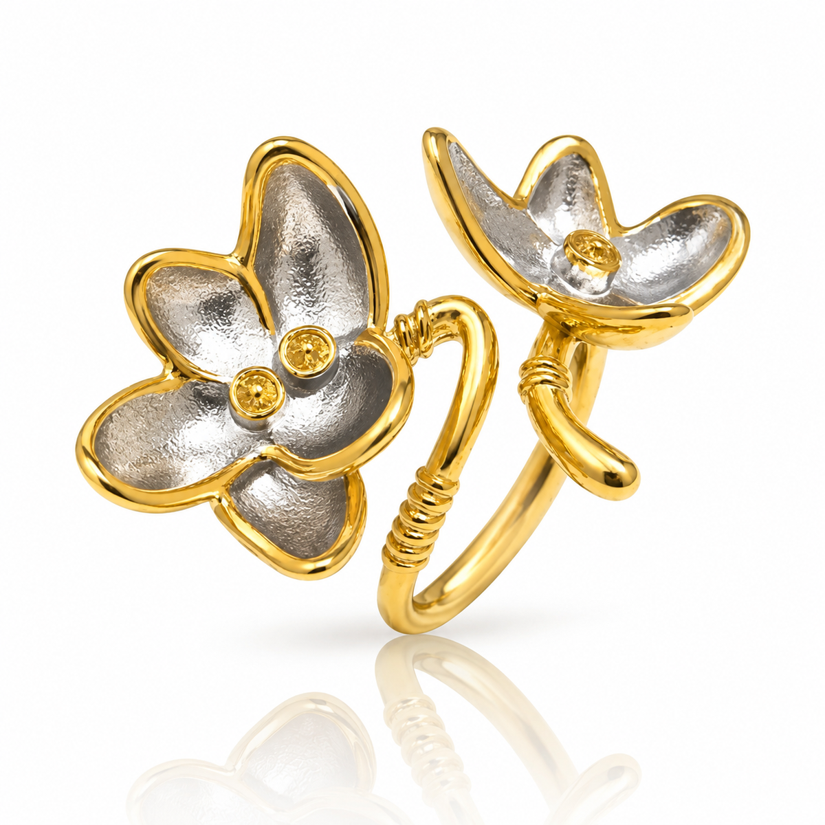 A two-tone gold and silver flower ring with small yellow gemstone accents, displayed on a clean white background with a soft reflection below.