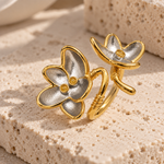 A pair of gold and silver flower-shaped rings displayed on a textured beige stone surface.