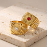 Two gold rings with heart-shaped gemstones on a beige stone surface
