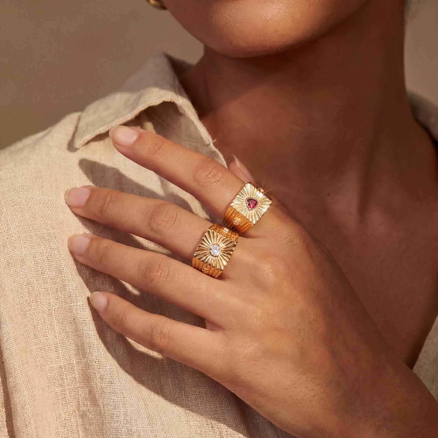 Close-up of a hand wearing two gold rings with gemstones on a neutral background