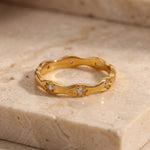 Gold ring with diamond accents on a beige stone surface