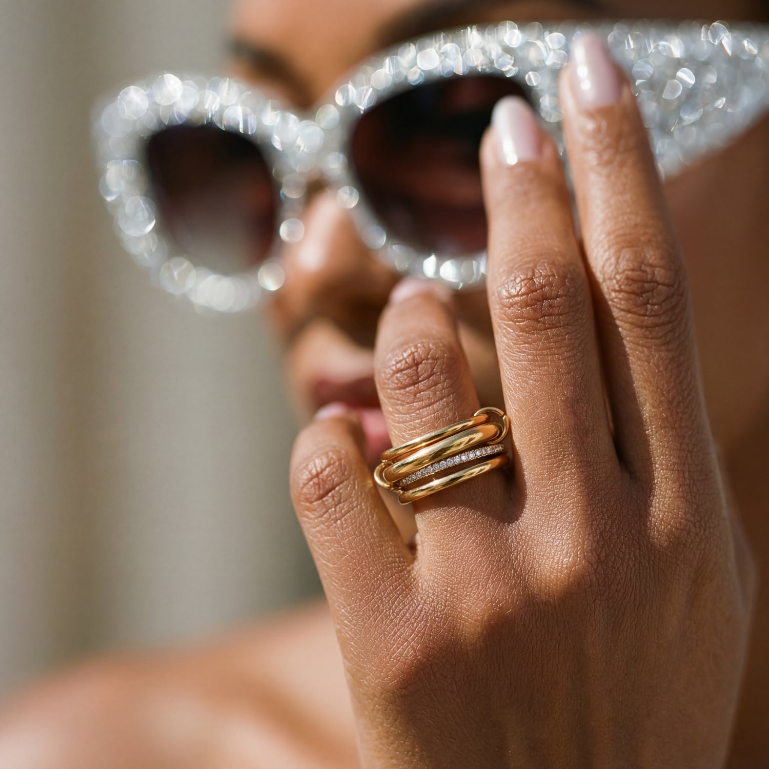 Person wearing sparkling sunglasses and a gold ring on a blurred background