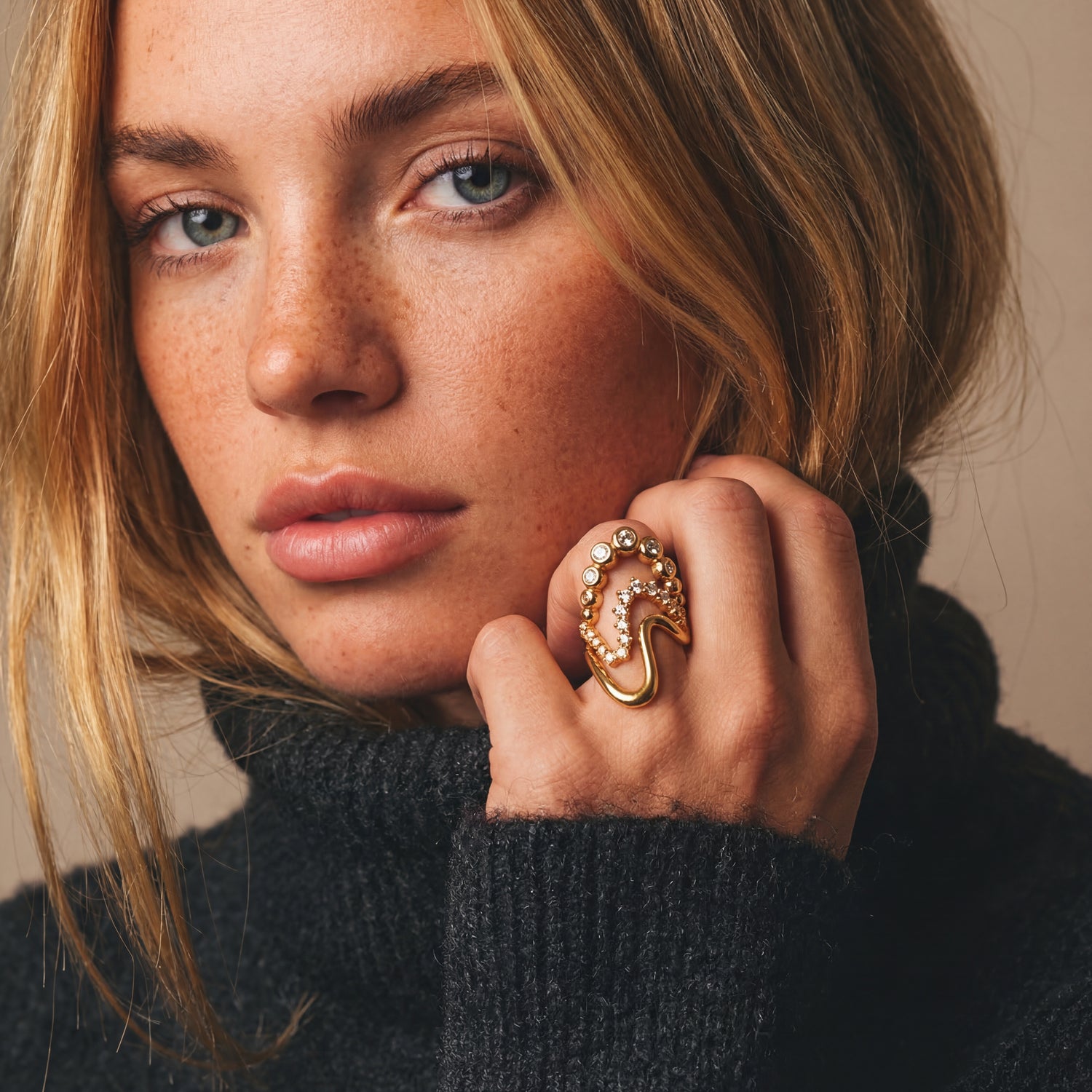 Woman wearing a gold ring with a unique design, against a neutral background