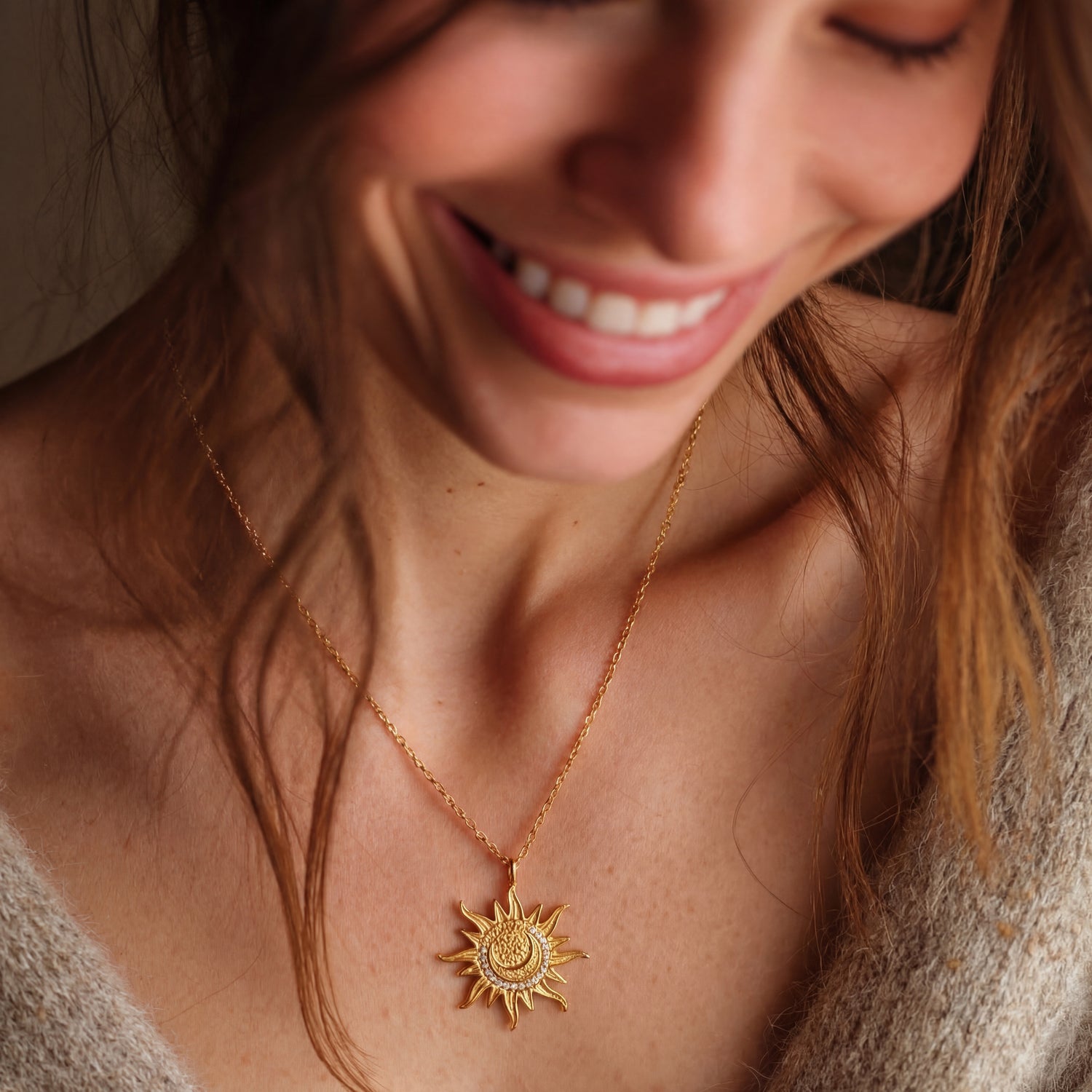 Woman wearing a gold necklace with a sun pendant, smiling.