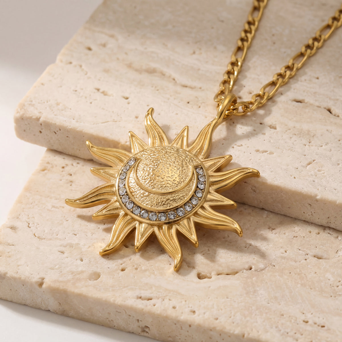 Gold sun-shaped necklace with embedded stones on a beige stone surface