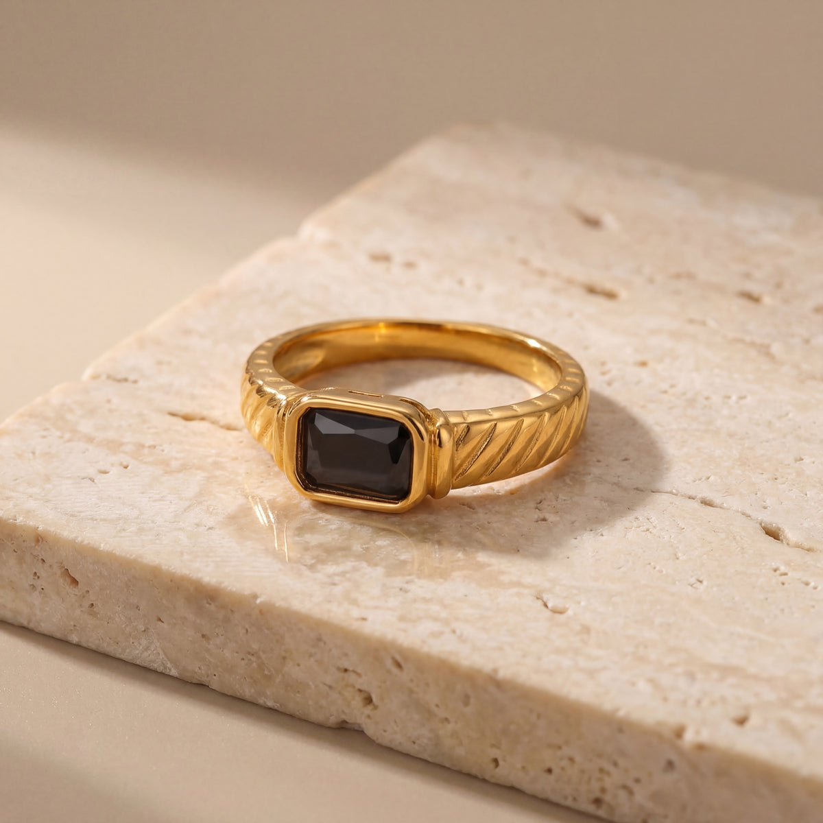 Gold ring with a black gemstone on a beige stone surface