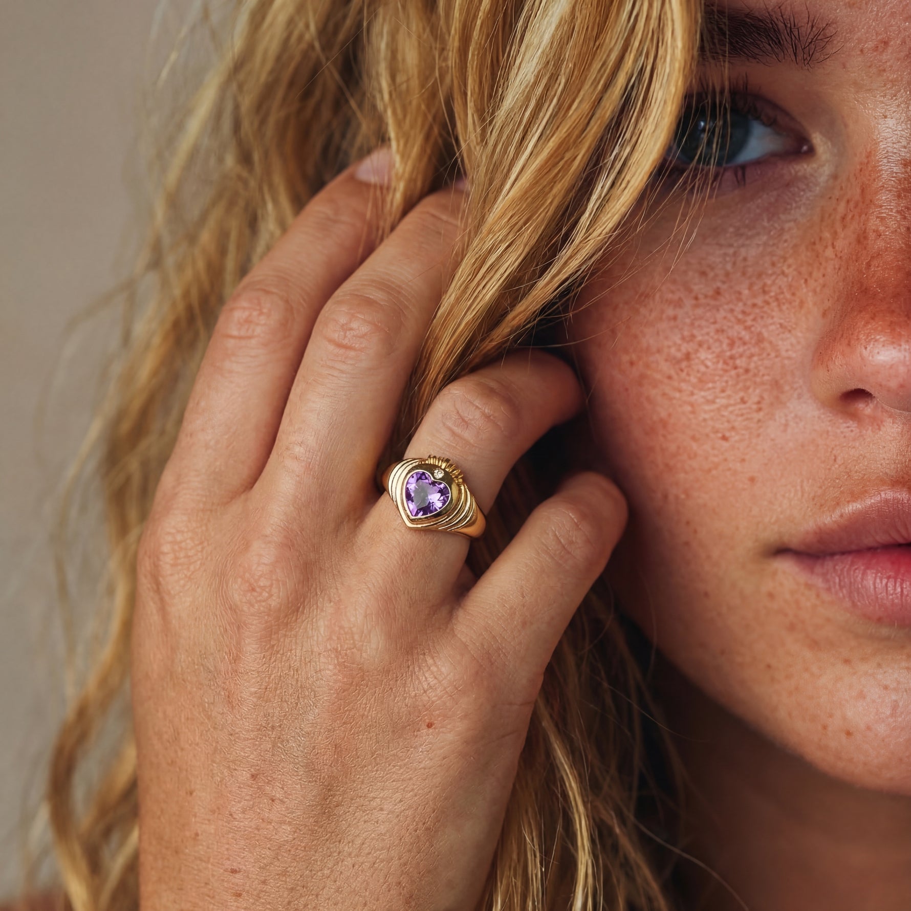 Close-up of a woman wearing a gold ring with a purple gemstone, touching her hair.