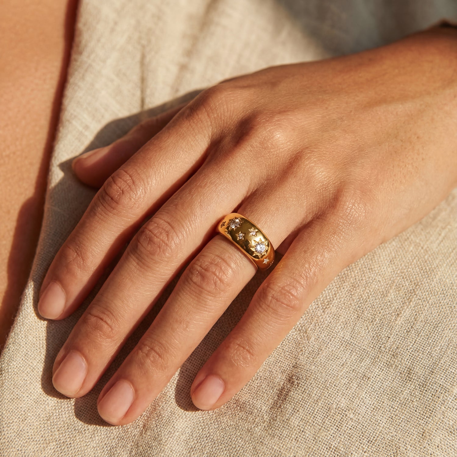 Close-up of a hand wearing a gold ring with gemstones on a beige fabric background