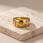 Gold ring with star and moon designs on a textured stone surface