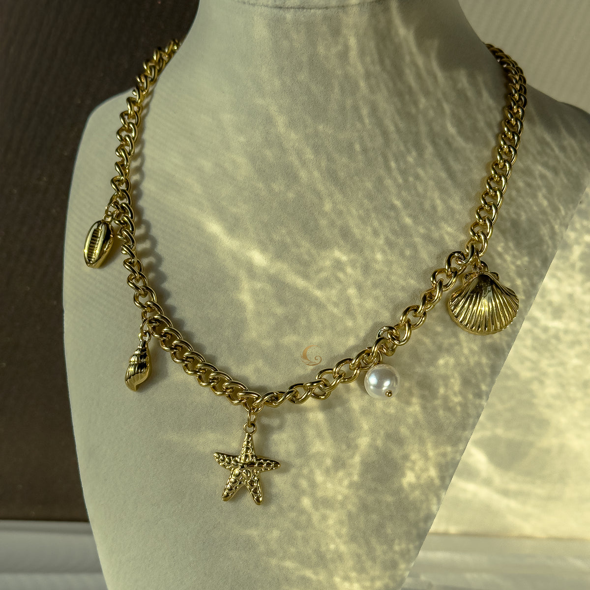 Halina necklace styled on mannequin bust, charms catching sunlight and casting soft reflections